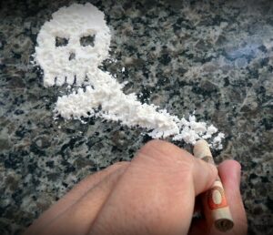 A picture of a skull made from cocaine powder with a hand holding a rolled up bill