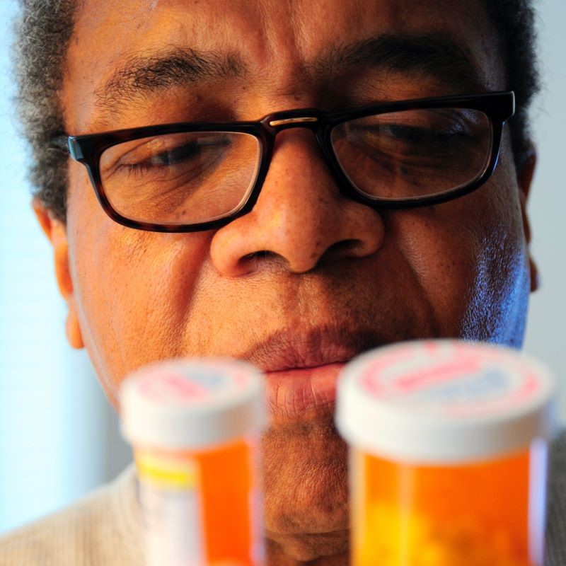 African American man with glasses looking at the labels of two prescription bottles